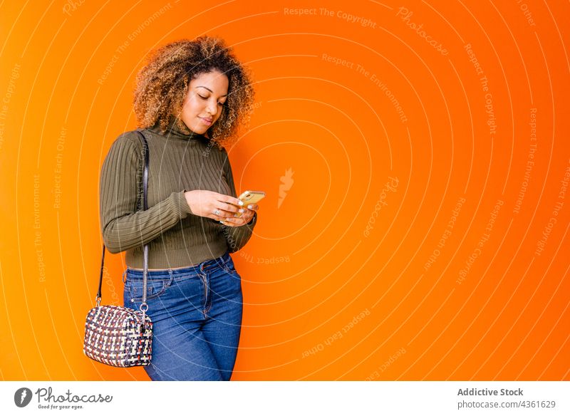 Afro-Frau, die ein Handy mit einer orangefarbenen Wand benutzt Afro-Look Person plaudernd Mobile Telefon Technik & Technologie Afrikanisch Hintergrund Internet