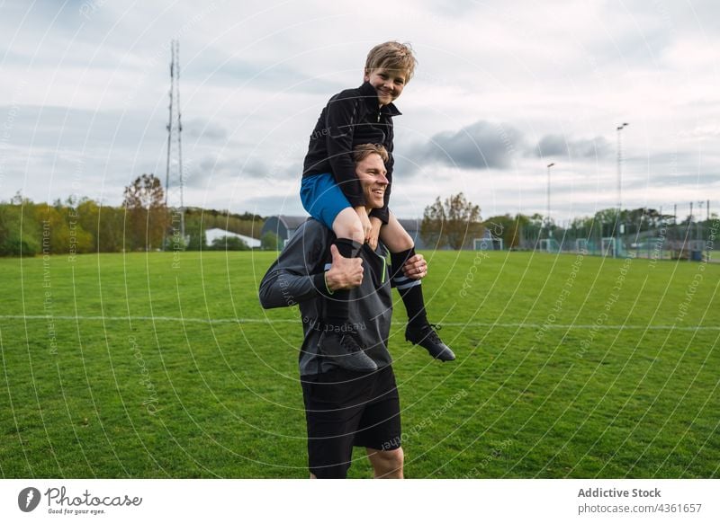 Vater und Sohn spielen Fußball auf einem Feld Zusammensein tragen Schulter Teenager Spieler Junge Aktivität Spaß haben Gras Eltern Vaterschaft Elternschaft