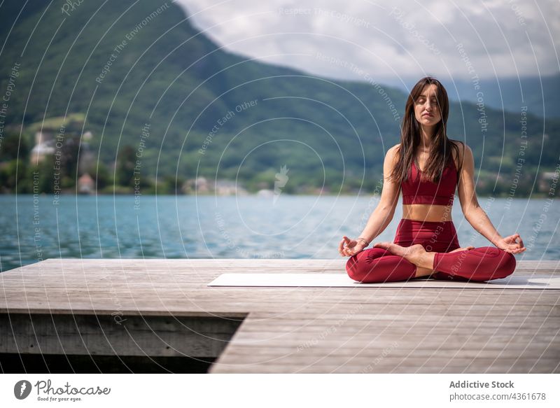Flexible Frau meditiert in Lotus-Pose auf dem Pier meditieren Yoga padmasana See Gelassenheit üben Asana Wasser Gesundheit ruhig sitzen Vitalität Wohlbefinden