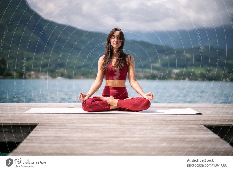 Flexible Frau meditiert in Lotus-Pose auf dem Pier meditieren Yoga padmasana See Gelassenheit üben Asana Wasser Gesundheit ruhig sitzen Vitalität Wohlbefinden