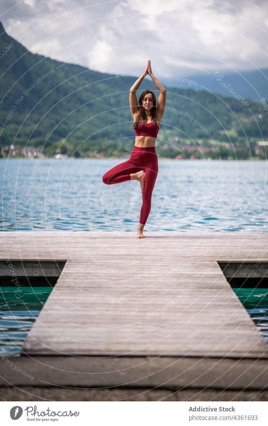 Schlanke Frau macht Yoga in Baumhaltung am Pier üben See Gleichgewicht vrksasana Asana beweglich Wellness Arme hochgezogen Teich Natur Kai Vitalität