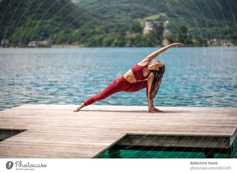 Frau, die Yoga in erweiterter Seitenwinkelhaltung auf dem Pier macht erweiterte Seitenwinkelstellung üben beweglich Dehnung See utthita parshvakonasana Asana