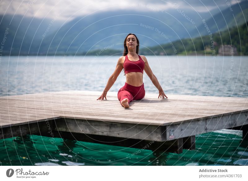 Flexible Frau in Front-Split-Pose sitzend und Yoga machend Dehnung beweglich Pier See üben ruhig Windstille Asana hanumanasana Harmonie Wasser Gelassenheit Kai