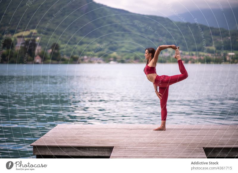 Flexible Frau beim Yoga in Lord of the Dance Pose am Kai Gleichgewicht üben tuladandasana See Pier Asana virabhadrasana Wasser ruhig Windstille Vitalität Zen