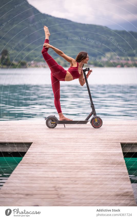 Lächelnde Frau macht Yoga im Stehenden Bogen Pose auf elektrischen Roller stehende Bogenhaltung üben Tretroller Gleichgewicht Natarajasana beweglich Gesundheit