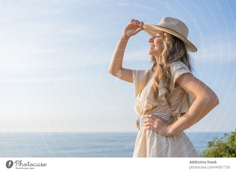 Glückliche Frau in stilvollem Sommeroutfit steht am Meer Mode Aussehen Kleid Hut MEER Augen geschlossen Stil Urlaub Feiertag jung charmant genießen reisen
