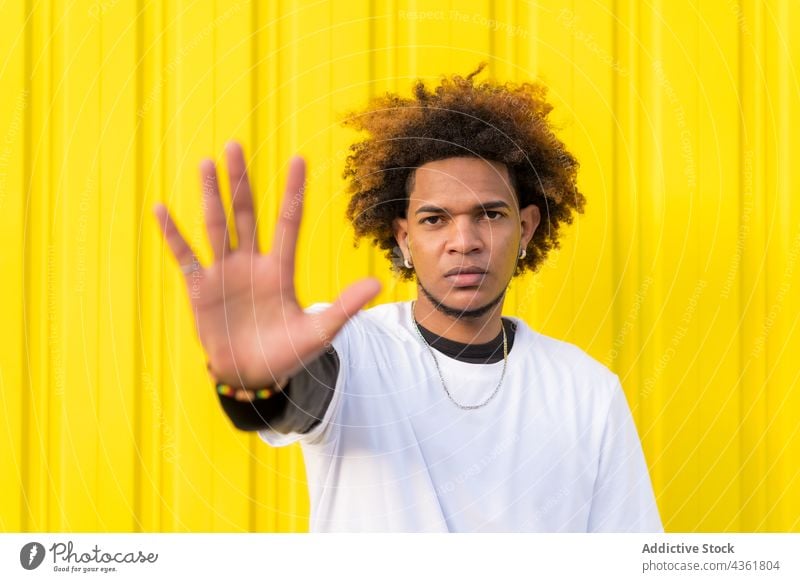 Schwarzer Mann zeigt Stopp-Geste gegen gelbe Wand stoppen gestikulieren Zeichen verbieten ablehnen verboten nein verweigern ernst männlich ethnisch schwarz
