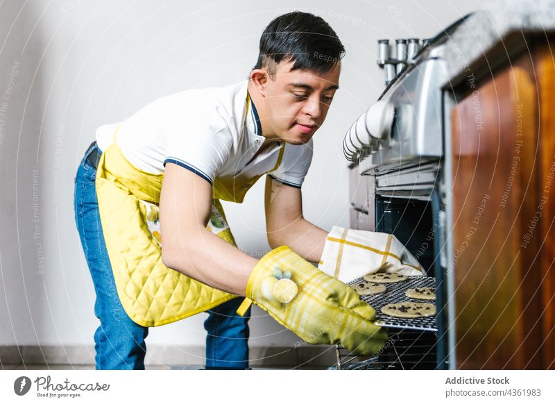 Lateinischer Teenager mit Down-Syndrom bereitet in der Küche Kekse zu Junge Koch Ofen vorbereiten Erkrankung mental Dessert ethnisch Gebäck süß backen