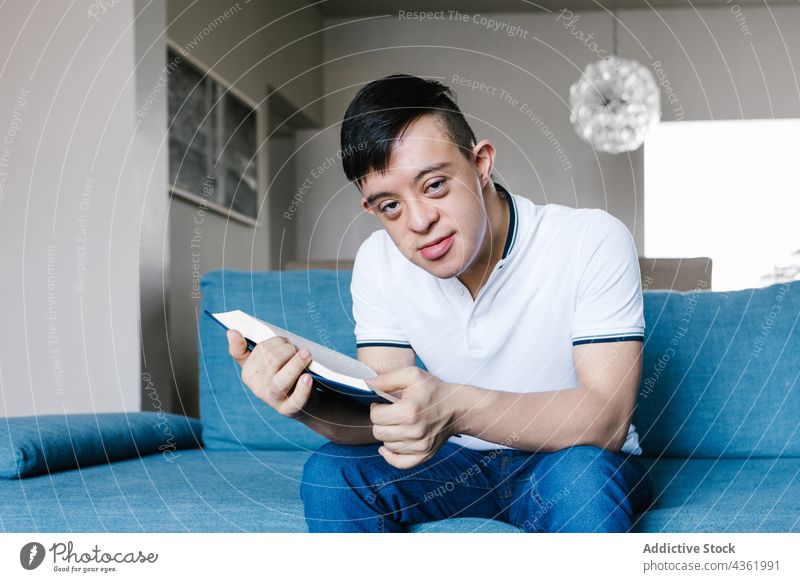 Lateinischer Junge mit Down-Syndrom liest zu Hause ein Buch lesen Teenager interessant Literatur heimwärts Sofa Hobby ethnisch Liege sitzen Wohnzimmer Wissen