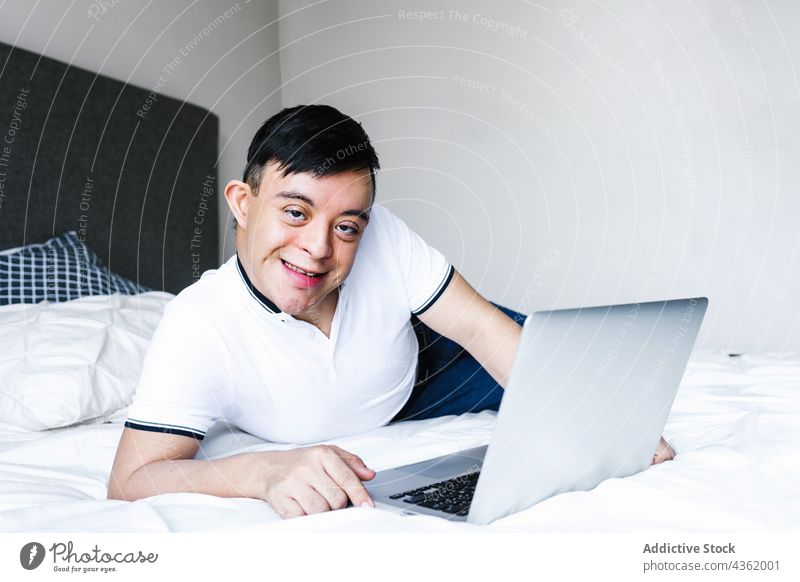 Ethnischer Teenager mit Down-Syndrom surft zu Hause auf seinem Laptop Junge Browsen Lügen Bett Surfen benutzend heimwärts ethnisch Latein unterhalten Apparatur