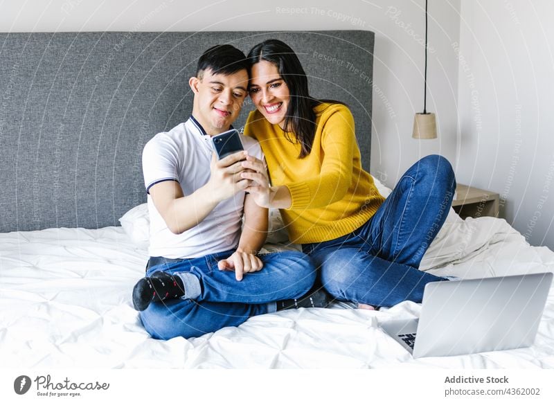 Fröhliche lateinamerikanische Mutter und Sohn mit Down-Syndrom machen ein Selfie zu Hause Selbstportrait Smartphone heimwärts Moment Zusammensein Liebe ethnisch