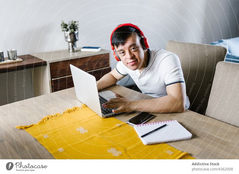 Lächelnder ethnischer Teenager mit Down-Syndrom, der während eines Fernstudiums einen Laptop benutzt Junge lernen heimwärts abgelegen Bildung Browsen Erkrankung