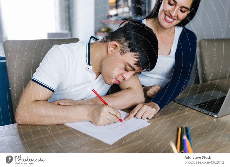 Lateinischer Junge mit Down-Syndrom, der mit seiner Mutter am Tisch zeichnet zeichnen Papier kreativ Sohn Zusammensein unterhalten Erkrankung ethnisch
