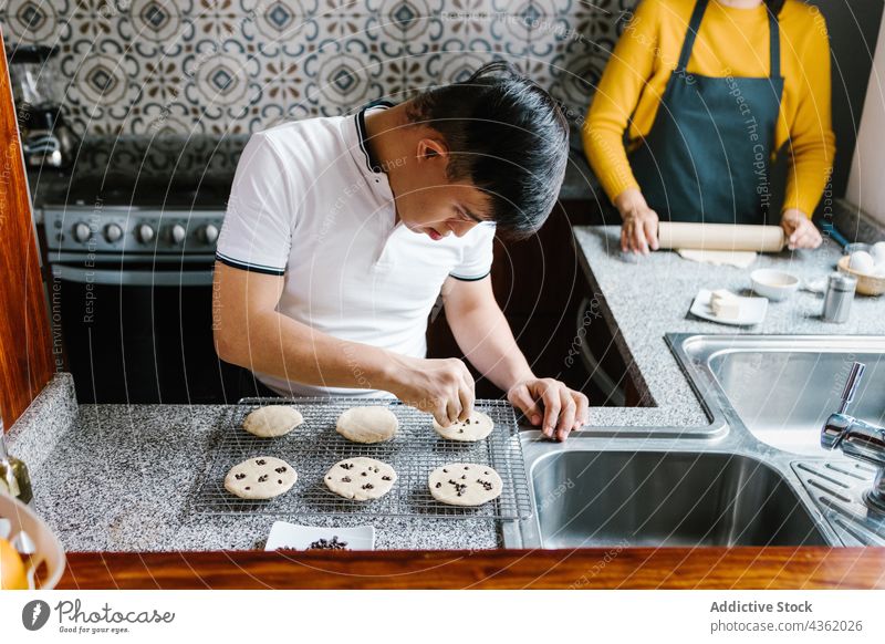 Ethnischer Junge mit Down-Syndrom bereitet in der Küche Kekse zu Koch Schokolade Chip vorbereiten Bäckerei roh ethnisch Latein Teenager süß Tisch frisch