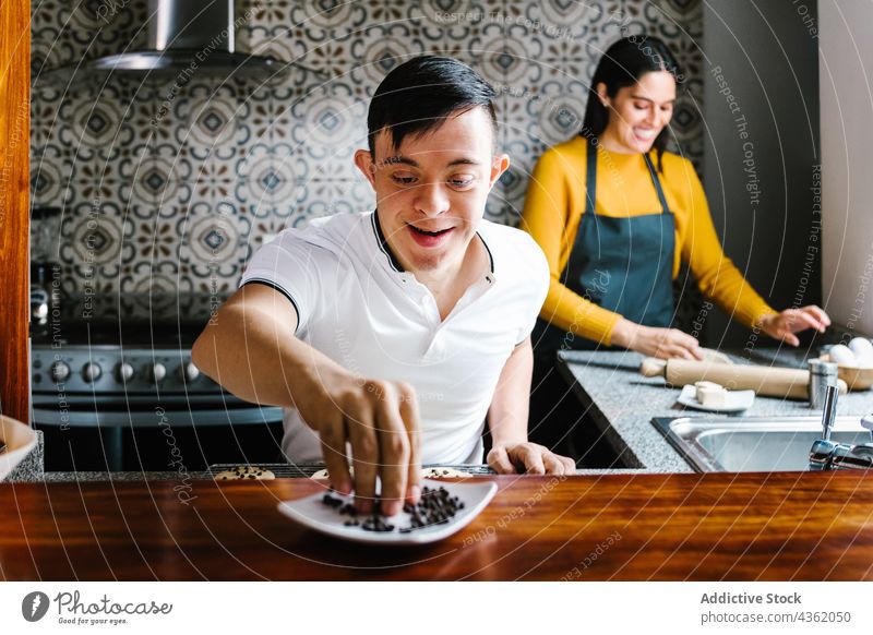 Fröhlicher lateinischer Junge mit Down-Syndrom kocht mit seiner Mutter in der Küche Koch Zusammensein Keks vorbereiten Bäckerei heiter Latein ethnisch Sohn