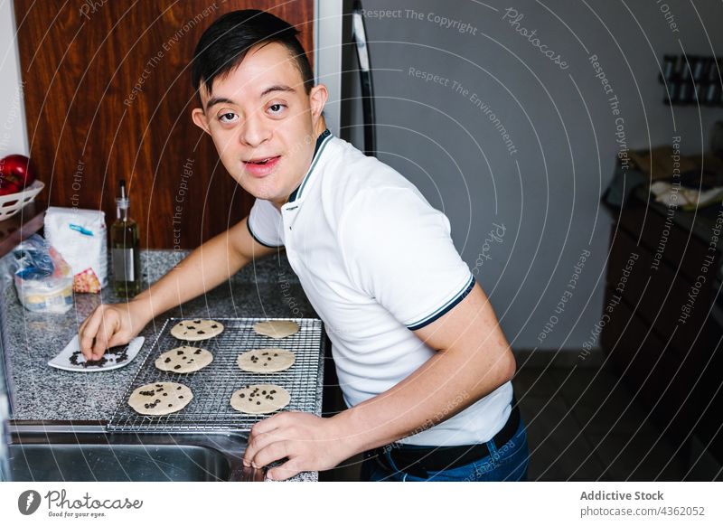 Glücklicher ethnischer Junge mit Down-Syndrom bei der Zubereitung von Keksen in der Küche Koch Schokolade Chip vorbereiten Bäckerei roh Latein Teenager süß