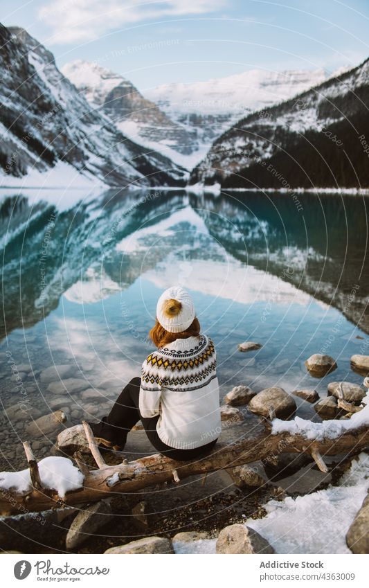 Unerkennbare Frau Reisende sitzt in der Nähe von ruhigen See Reisender Ufer ruhen Berge u. Gebirge sitzen Natur Wasser Winter Lake Luise Banff National Park