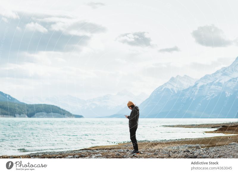 Frau benutzt Smartphone in der Nähe eines Sees Reisender benutzend Ufer wolkig tagsüber Natur Wasser Abrahamsee Banff National Park Alberta Kanada reisen