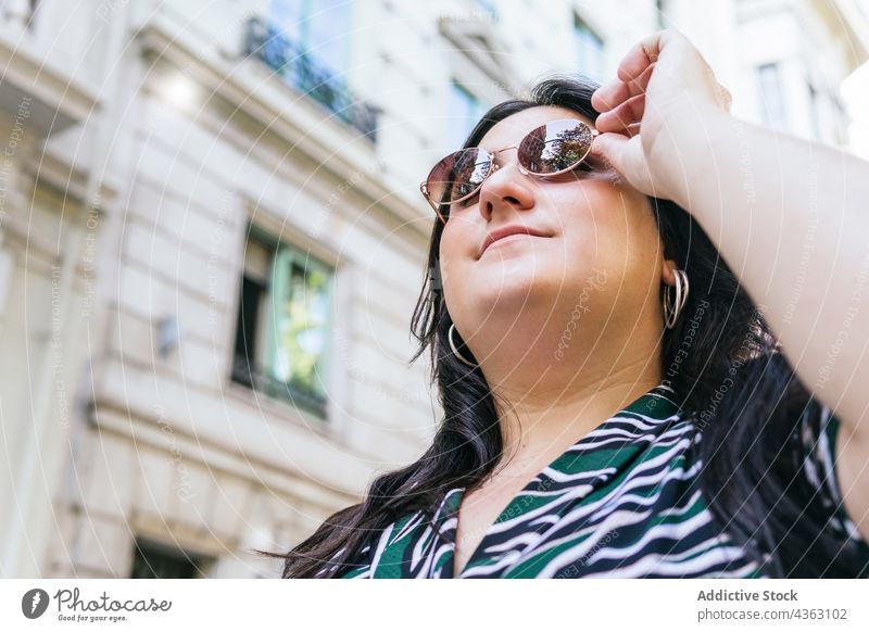 Stilvolle Frau mit Sonnenbrille auf einer Straße in der Stadt trendy Mode Sommer urban Kleid kurvenreich Aussehen jung Übergröße Brille Outfit drucken