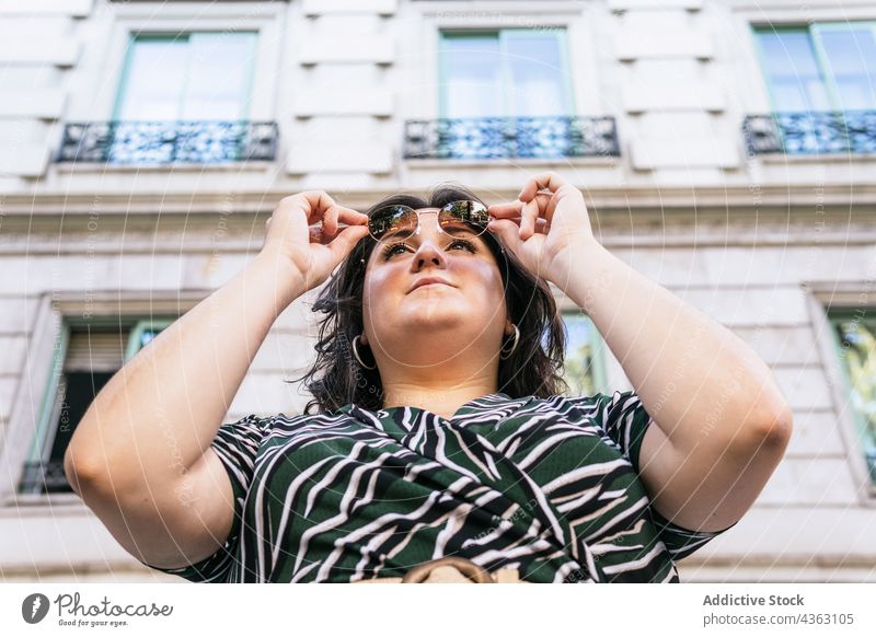 Stilvolle Frau mit Sonnenbrille auf einer Straße in der Stadt trendy Mode Sommer urban Kleid kurvenreich Aussehen jung Übergröße Brille Outfit drucken