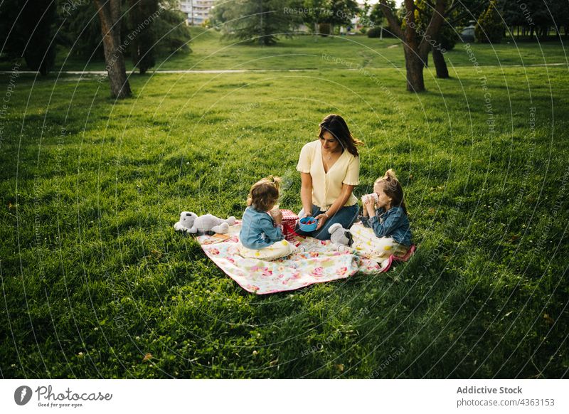 Fröhliche Mutter und Kinder beim Picknick im Park Zusammensein Sommer Glück Liebe Tochter Geschwisterkind trinken Tasse Mama Partnerschaft wenig Schwester