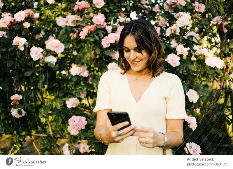 Glückliche Frau mit Smartphone im blühenden Garten Blume benutzend Blütezeit Apparatur Mobile Telefon Gerät Browsen jung Lächeln Kommunizieren Frühling
