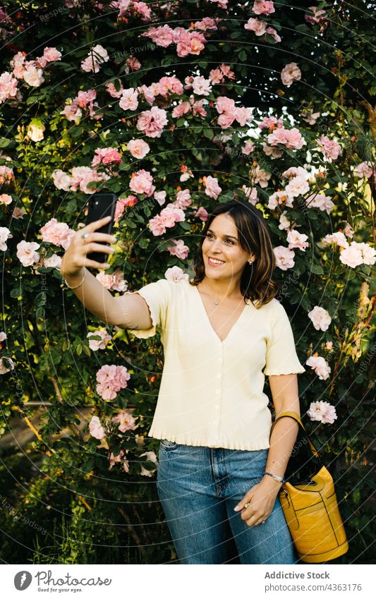 Glückliche Frau mit Smartphone im blühenden Garten Blume benutzend Blütezeit Apparatur Mobile Telefon Gerät Browsen jung Lächeln Kommunizieren Frühling