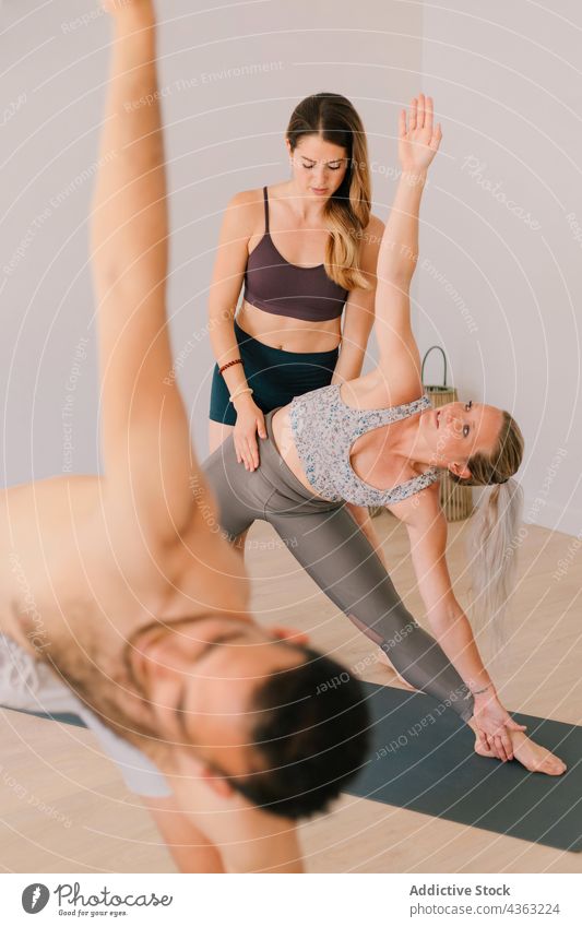 Yogalehrer hilft der Gruppe während des Unterrichts Trainerin Menschengruppe Klasse Hilfsbereitschaft abstützen Ausbilderin Zusammensein üben Krieger-Pose Asana