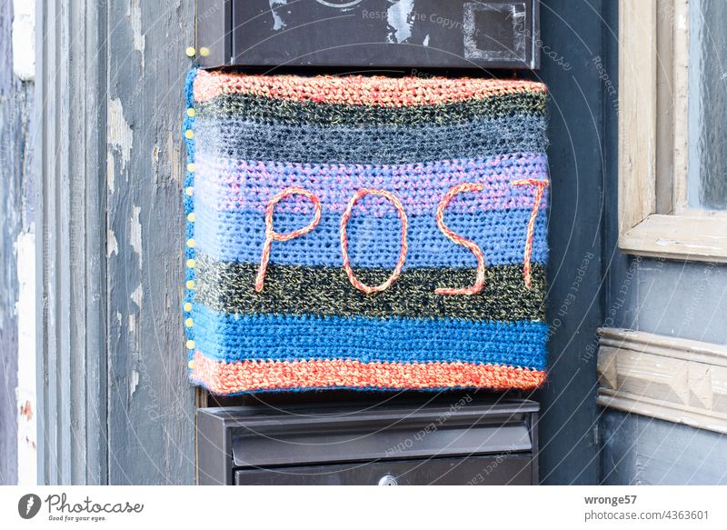 Nahaufnahme eines mit farbigen Garn bunt bestrickter Briefkasten mit der Aufschrift POST an einem Fachwerkhaus Postkasten Farbig urban knitting Verschönerung