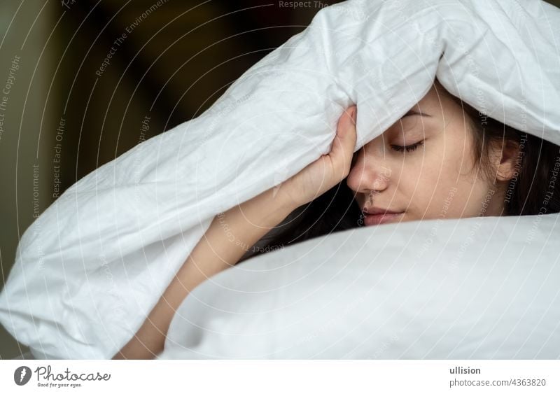 Porträt einer attraktiven, jungen, sexy dunkelhaarigen Frau im Bett, Hand und Kopf auf dem Kissen unter der Decke, Raum kopieren. schlafen Menschen weiß