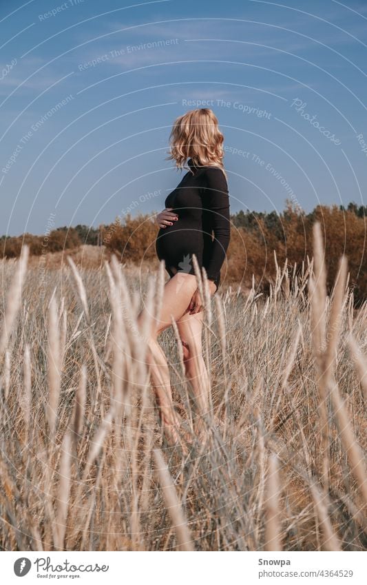 Junge, blonde schwangere Frau am Strand gebogen Gras trägt schwarzen Body halten Schwangerschaft Bauch. Freiraum. Mutterschaft. Sommer Schwangerschaft Konzept.