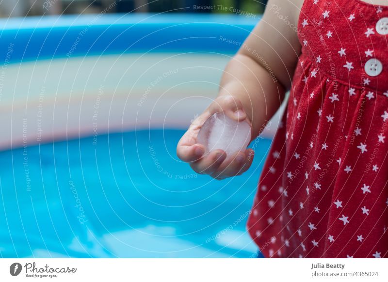 Ein Jahr altes Baby bei einem sensorischen Spiel mit Eiswürfeln in einem aufblasbaren Pool im Sommer berühren Halt kalt spielen Kind Erfahrung lernen wachsen