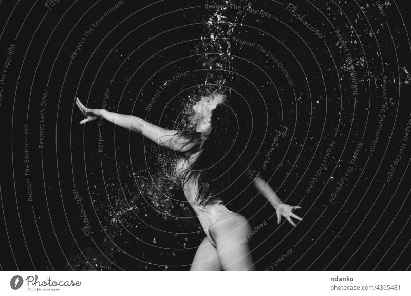Junge schöne Frau kaukasischen Aussehens mit langen Haaren tanzt in Wassertropfen auf einem schwarzen Hintergrund. Springen und schwingen die Arme Aktion aktiv