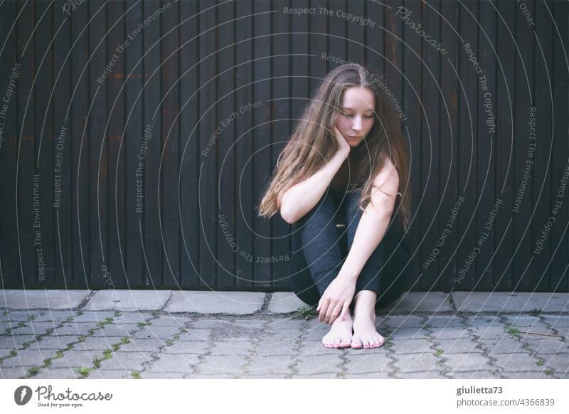 Porträt eines Teenager Mädchens, draussen auf dem Boden sitzend, allein, traurig, hoffnungslos Pubertät langhaarig Hintergrund neutral Liebeskummer Traurigkeit