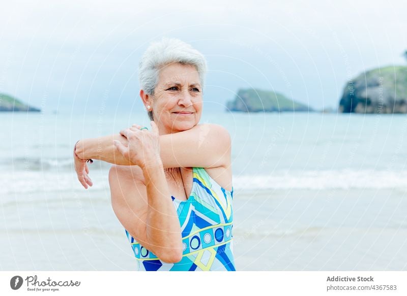 Glückliche ältere Frau beim Sport am Meer Senior Übung Training Strand Gesunder Lebensstil Dehnung Schulter MEER Badeanzug Arme Aktivität Wohlbefinden Stil