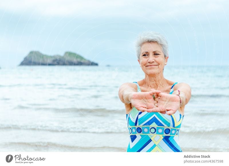 Ältere Frau im Badeanzug streckt Arme am Strand aus Senior Übung Training Gesunder Lebensstil Dehnung MEER Aktivität Wohlbefinden Stil graues Haar alt Meer