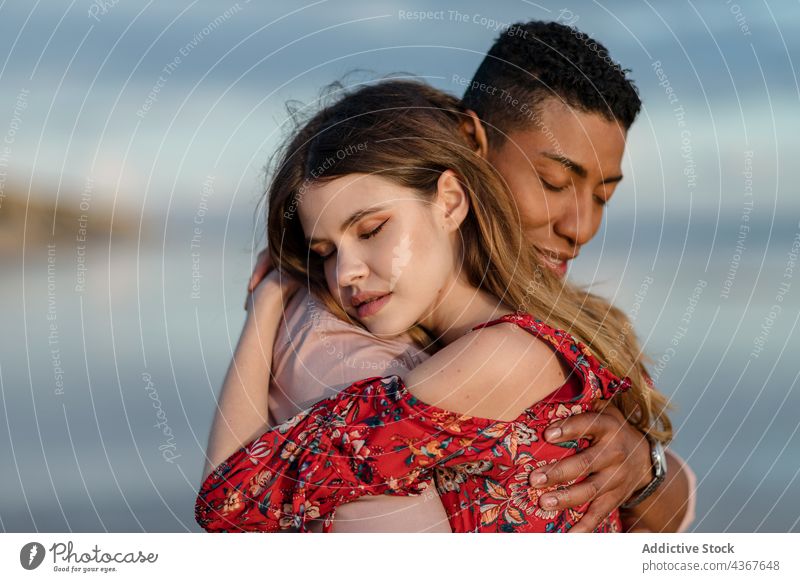 Zärtliches multiethnisches Paar umarmt sich am Strand Umarmen Liebe Meeresufer Angebot Gelassenheit Umarmung Partnerschaft rassenübergreifend vielfältig schwarz