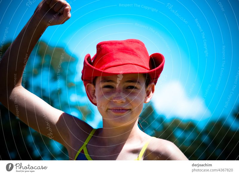 So sehen Sieger aus. Junges Girl mit rotem Hut, reckt die rechte Hand nach oben. Im Hintergrund blauer Himmel und kleine weiße Wolken. sieger Farbfoto