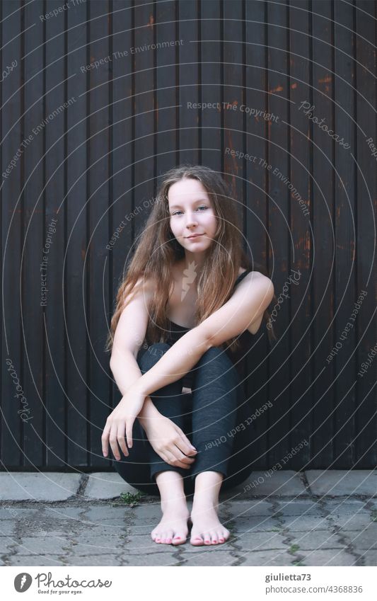Porträt eines Teenager Mädchens mit langen Haaren, cool, lächelnd, draussen auf dem Boden sitzend Außenaufnahme Blick in die Kamera Jugendliche Vorderansicht