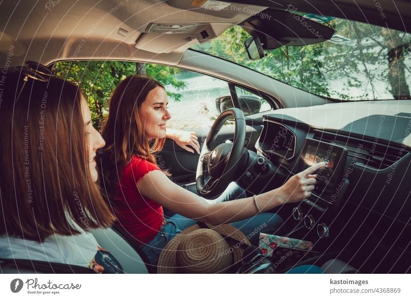 Zwei junge Mädchen hören gute Musik, während sie im Auto fahren und den Sommerausflug in der Natur genießen. Ausflug Straße PKW Zusammensein reisen Frau Urlaub