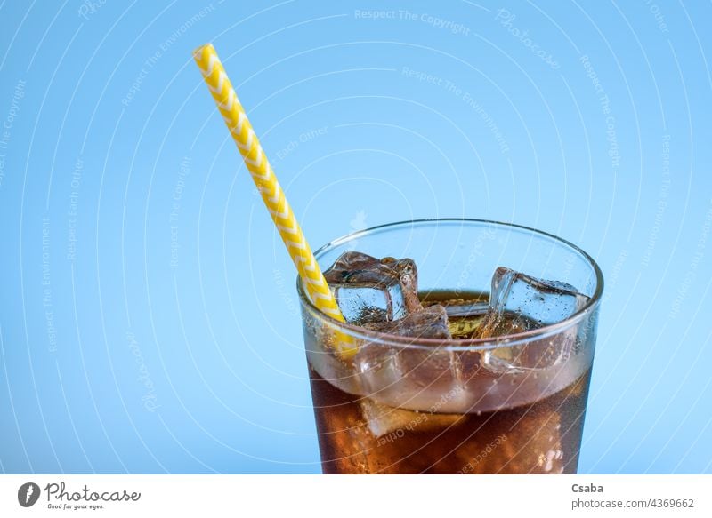 Ein Glas Cola mit Eis auf blauem Hintergrund Soda weich trinken kalt Stroh Sommer Erfrischung Koffein liquide braun Getränk Kondenswasser Tau Würfel