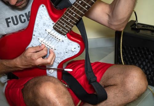 Unbekannter Mann sitzt auf dem Boden und spielt eine rote E-Gitarre. Gitarrenspieler spielen Person unverschämt männlich Felsen Punk lässig alternativ Musiker