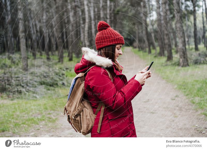 Seitenansicht von Backpacker kaukasische Frau zu Fuß im Wald mit Handy im Winter oder Herbst Saison. Lebensstil und Natur. Weitwinkelansicht