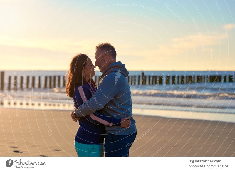 Romantisches Paar mittleren Alters, das sich an einem tropischen Strand bei Sonnenuntergang umarmt und sich liebevoll in die Augen schaut, mit seitlichem Kopierraum