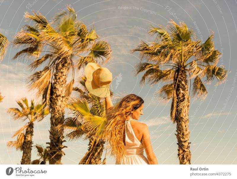Portrait schöne Frau tanzen hält Sonnenhut am Strand Palmen Hintergrund.Sommerurlaub Konzept Lebensstil Handfläche Tanzen Kleid weiß Mode Person Sand jung MEER