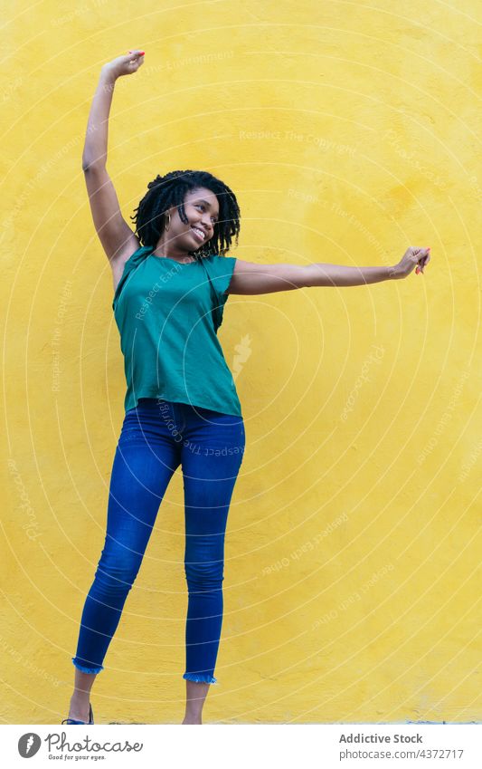 Lachende junge Afrikanerin vor gelber Wand mit erhöhtem Afrikanisch Menschen Glück Porträt Frau Amerikaner Model Dame Ethnizität Afro-Look Lächeln Mädchen schön
