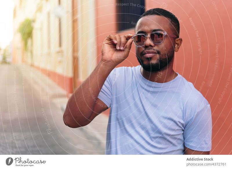 Afrikanischer Mann mit Sonnenbrille, der auf einer Straße in der Stadt geht und in die Kamera schaut. selbstbewusst männlich Erwachsener Amerikaner schwarz
