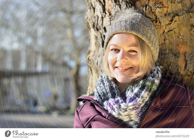 Junge blonde Frau lehnt an Baum | naturverbunden Blick in die Kamera Vorderansicht Tag Lebensfreude positiv natürlich schön Fröhlichkeit Lächeln genießen
