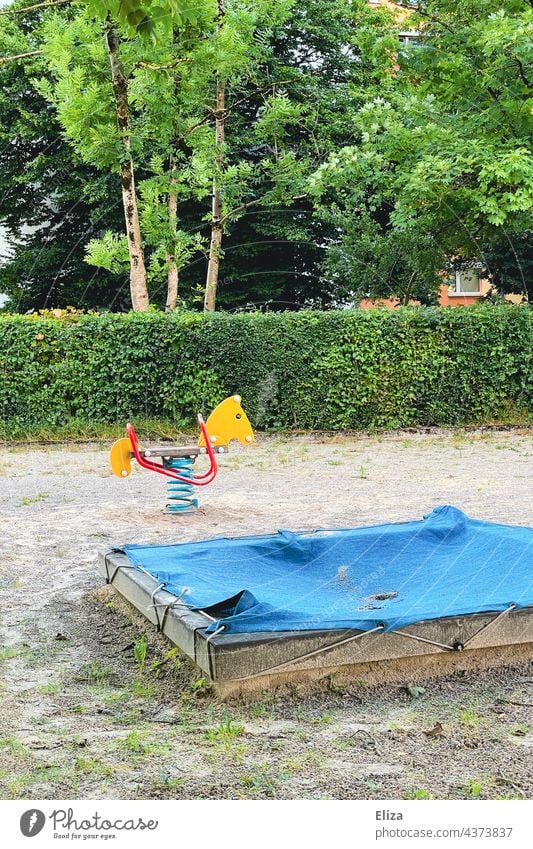 Abgedeckter Sandkasten und Schaukelpferd auf einem Kinderspielplatz abgedeckt Spielplatz Kindheit Spielmöglichkeit Plane blau geschlossen Kindergarten