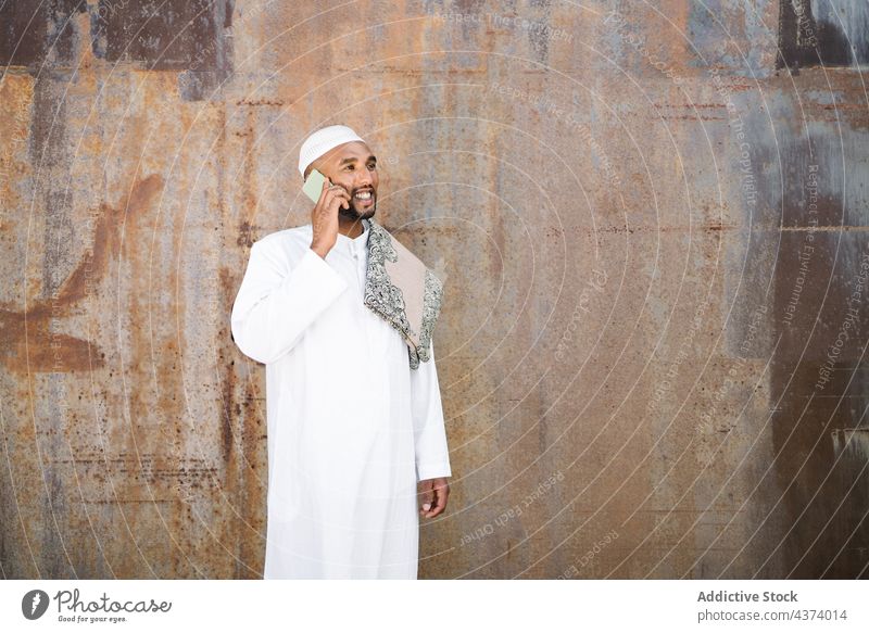 Islamischer Mann benutzt Smartphone auf der Straße muslimisch arabisch benutzend Lächeln Tradition Wand schäbig soziale Netzwerke ruhen männlich Funktelefon